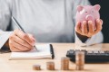 Foto: Hand mit Notizbuch und Sparschwein